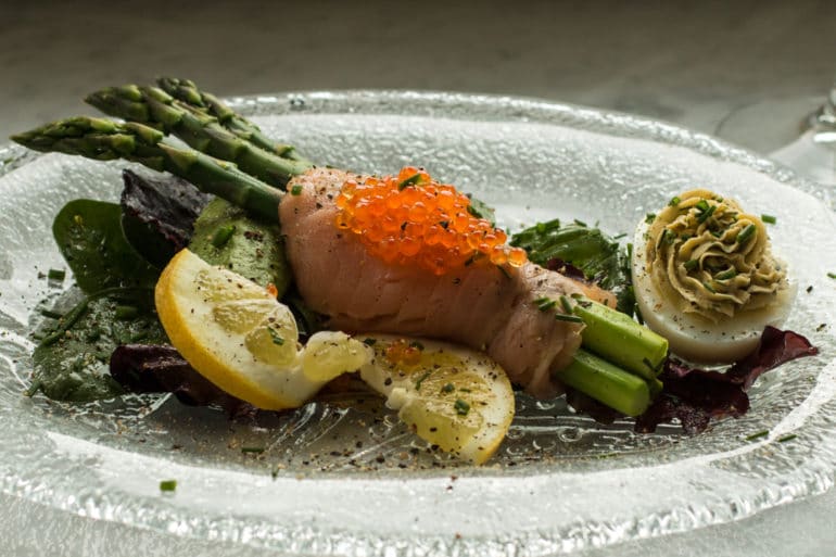 Plated asparagus wrapped in cold smoked salmon with a smoked salmon deviled egg. Plated asparagus wrapped in cold smoked salmon with a smoked salmon deviled egg.
