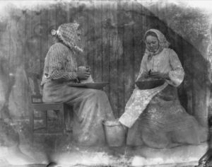 Two women are peeling potatoes with a bucket between them (circa 1904) Nils Keyland / CC0